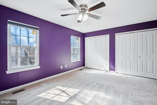 unfurnished bedroom featuring multiple closets, multiple windows, and light carpet