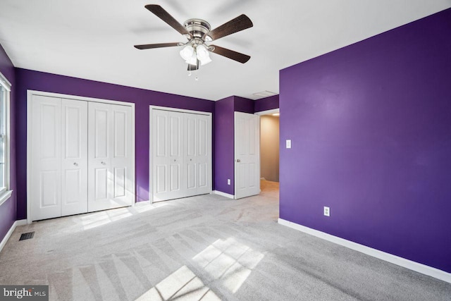 unfurnished bedroom featuring ceiling fan, light colored carpet, and two closets