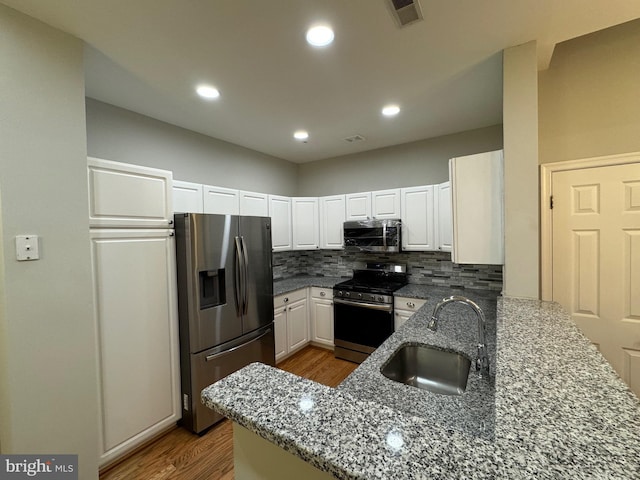 kitchen with sink, white cabinetry, stone countertops, kitchen peninsula, and stainless steel appliances