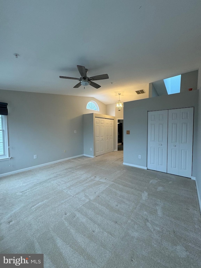 interior space featuring light carpet, two closets, vaulted ceiling, and ceiling fan