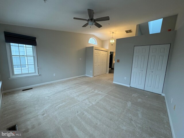 unfurnished bedroom with light carpet, ceiling fan, vaulted ceiling, and multiple closets