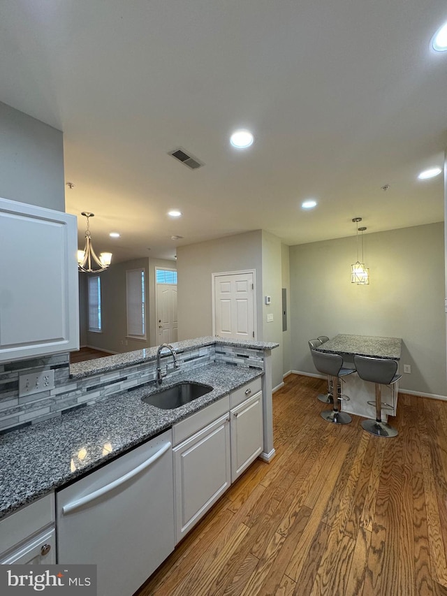 kitchen featuring sink, decorative light fixtures, dark stone countertops, dishwashing machine, and white cabinets