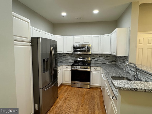 kitchen featuring stainless steel appliances, light stone countertops, sink, and white cabinets