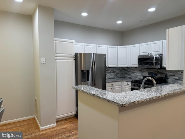 kitchen featuring white cabinetry, stainless steel appliances, kitchen peninsula, and light stone counters