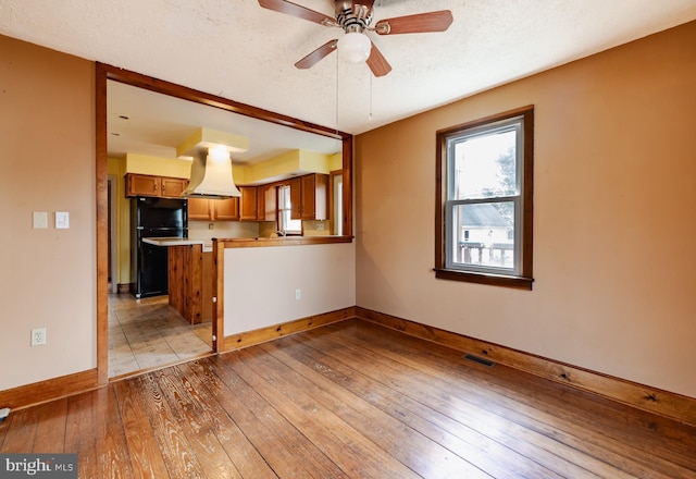 kitchen featuring black fridge, ventilation hood, a textured ceiling, kitchen peninsula, and light hardwood / wood-style floors