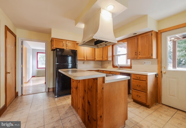 kitchen with a kitchen island, radiator, island range hood, a wealth of natural light, and black fridge