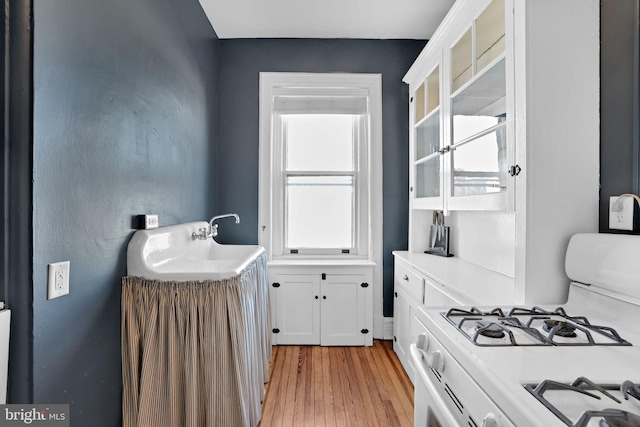 kitchen with sink, white range with gas stovetop, light hardwood / wood-style floors, and white cabinets