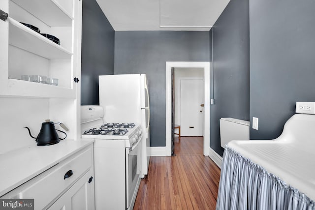 kitchen featuring wood-type flooring, white gas range oven, and white cabinets