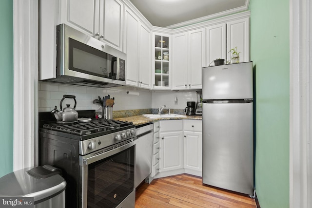 kitchen featuring appliances with stainless steel finishes, white cabinetry, tasteful backsplash, light stone countertops, and light hardwood / wood-style floors