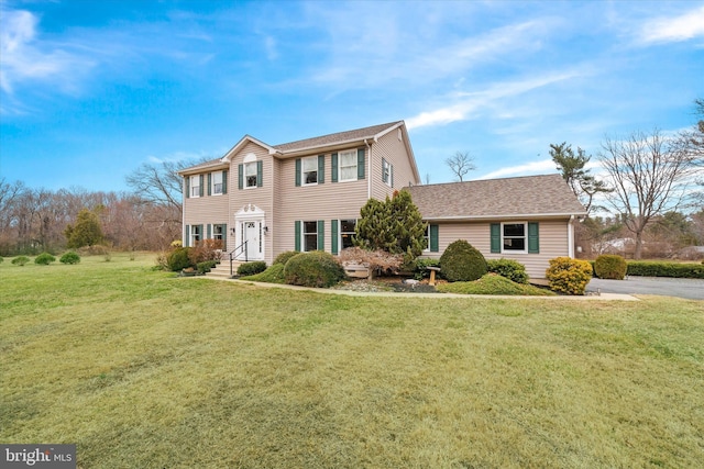 colonial-style house featuring a front yard and a shingled roof