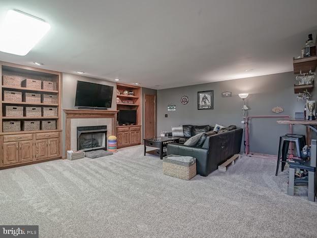 living room with light carpet, built in shelves, and a tiled fireplace