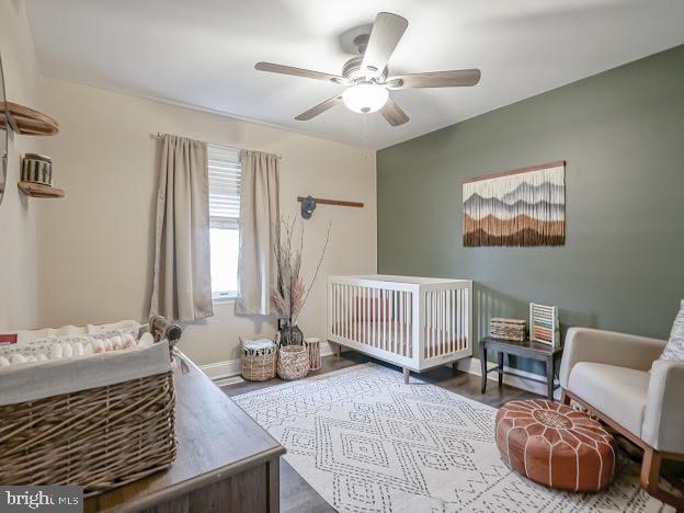 bedroom featuring ceiling fan, wood-type flooring, and a crib