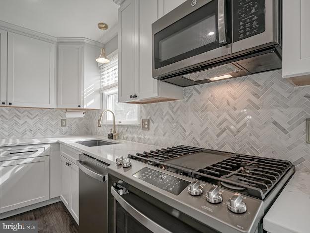 kitchen featuring sink, white cabinetry, hanging light fixtures, stainless steel appliances, and light stone countertops