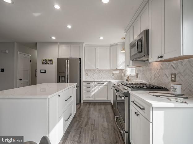 kitchen with appliances with stainless steel finishes, decorative light fixtures, wood-type flooring, white cabinets, and backsplash