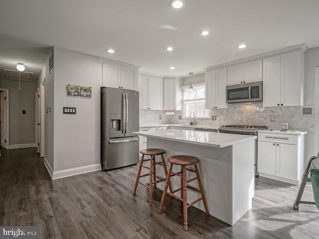 kitchen featuring a kitchen bar, white cabinetry, a center island, hanging light fixtures, and appliances with stainless steel finishes