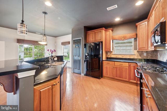 kitchen featuring sink, black appliances, a kitchen bar, decorative light fixtures, and light wood-type flooring