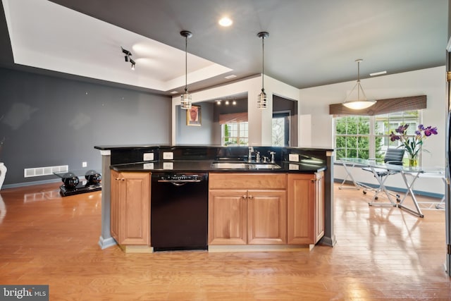 kitchen featuring a tray ceiling, dishwasher, sink, and hanging light fixtures