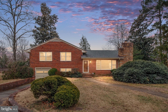 tri-level home featuring brick siding, a chimney, an attached garage, and a shingled roof