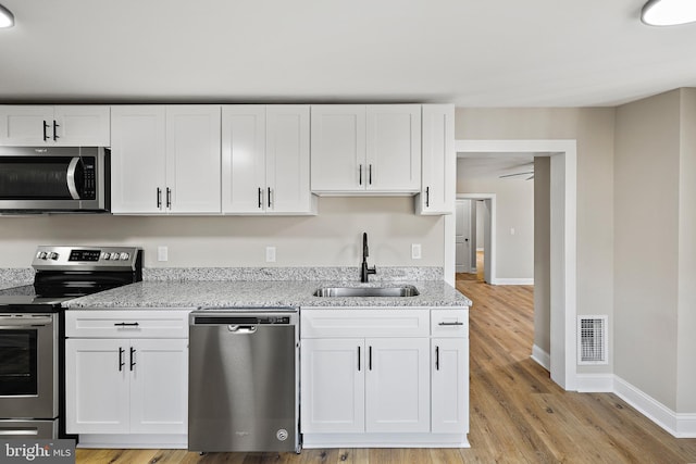 kitchen featuring sink, white cabinetry, light stone counters, light hardwood / wood-style flooring, and appliances with stainless steel finishes