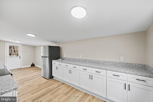 kitchen featuring light stone countertops, light hardwood / wood-style floors, stainless steel refrigerator, and white cabinets