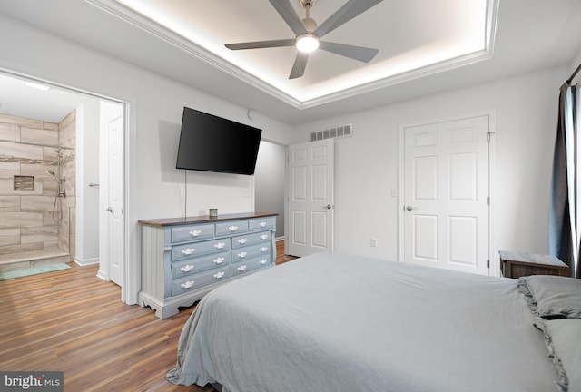 bedroom featuring hardwood / wood-style flooring, a raised ceiling, ceiling fan, and ensuite bathroom