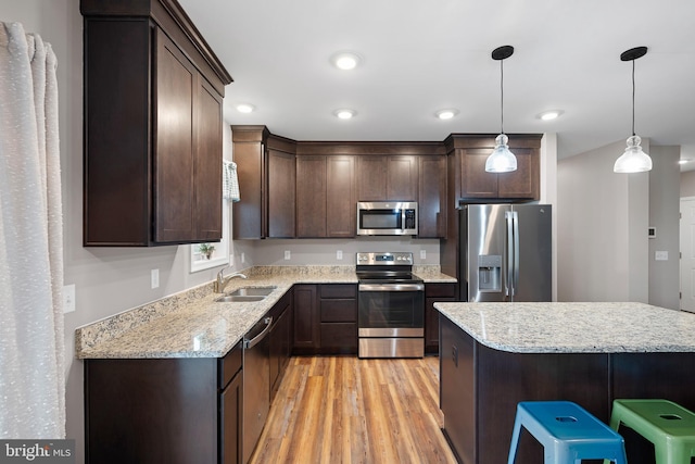 kitchen with sink, hanging light fixtures, a kitchen breakfast bar, stainless steel appliances, and light wood-type flooring