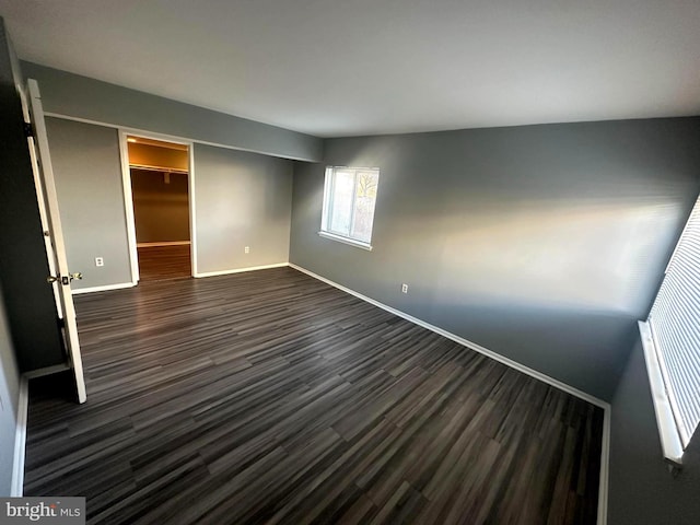 unfurnished bedroom with a closet, a walk in closet, and dark hardwood / wood-style floors