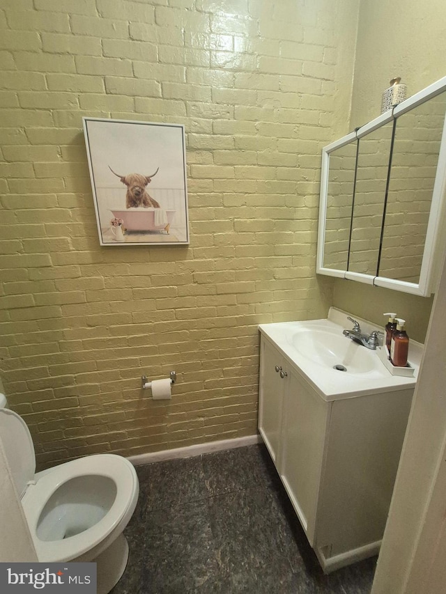 bathroom with vanity, brick wall, and toilet