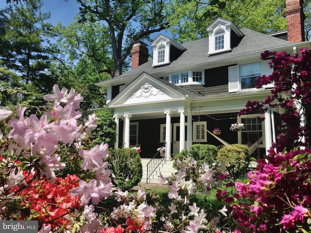 rear view of property with covered porch, a shingled roof, and a chimney