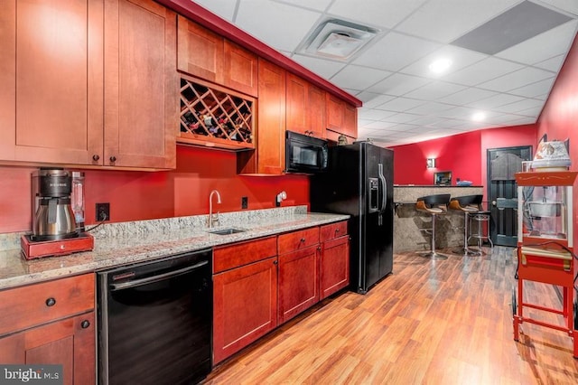 kitchen featuring sink, light hardwood / wood-style flooring, black appliances, light stone countertops, and a drop ceiling