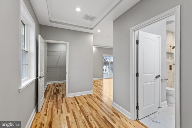 corridor with visible vents, a tray ceiling, recessed lighting, light wood finished floors, and baseboards