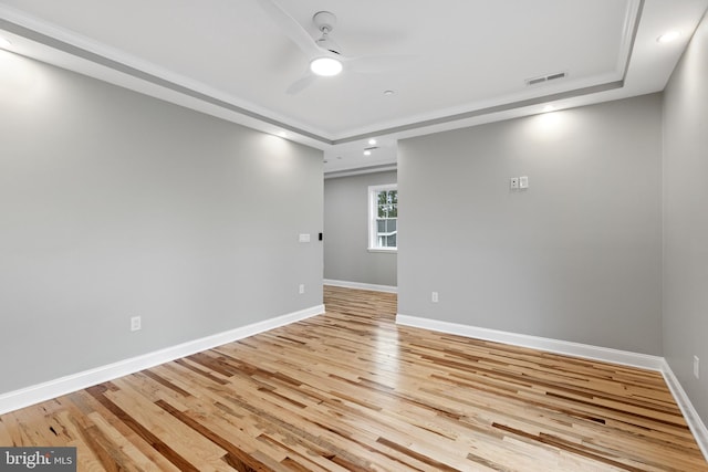 empty room with visible vents, a ceiling fan, baseboards, light wood-style floors, and a raised ceiling