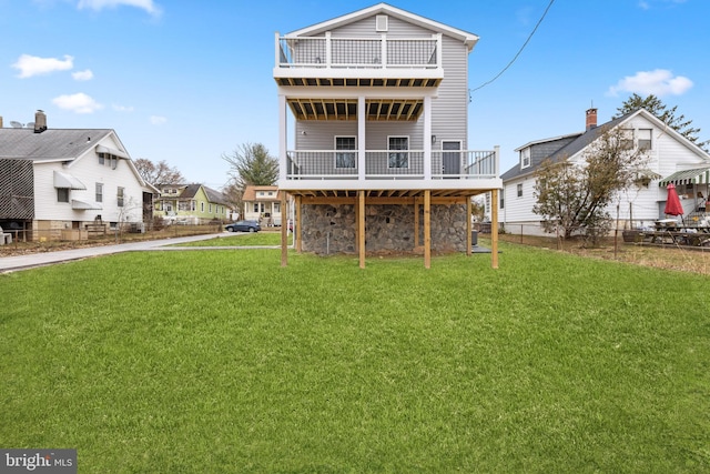 rear view of house featuring a deck, a yard, fence, and stone siding