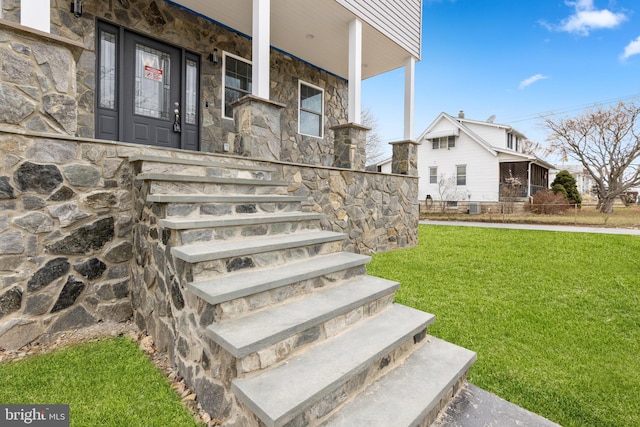 view of exterior entry with a porch, a yard, and stone siding