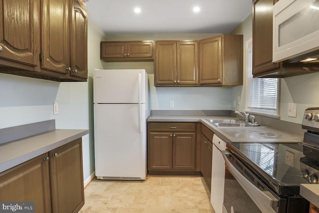 kitchen with white appliances, brown cabinets, light countertops, a sink, and recessed lighting