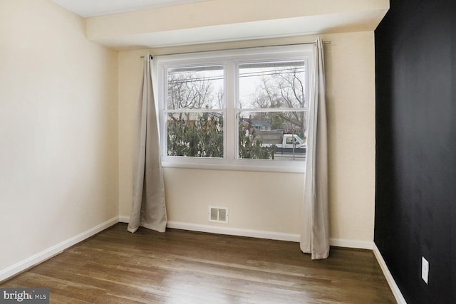 unfurnished room with dark wood finished floors, visible vents, and baseboards