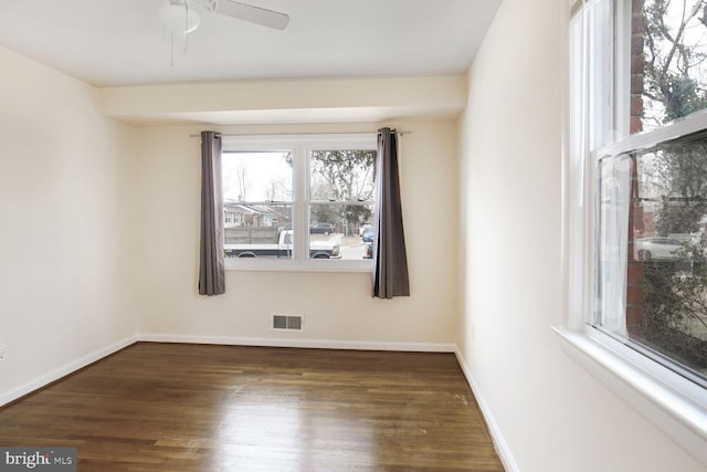 empty room with a ceiling fan, visible vents, dark wood finished floors, and baseboards