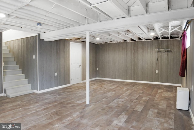 finished basement featuring stairs, wooden walls, baseboards, and wood finished floors