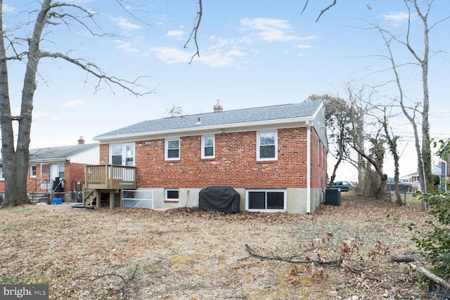 back of house with a shingled roof, a chimney, a deck, cooling unit, and brick siding