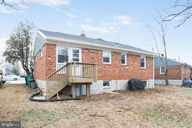 rear view of property with stairs, roof with shingles, brick siding, and a chimney