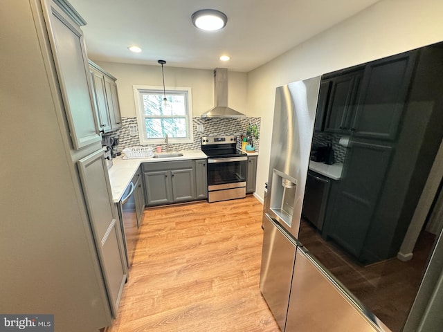 kitchen with decorative light fixtures, sink, stainless steel appliances, light wood-type flooring, and wall chimney exhaust hood