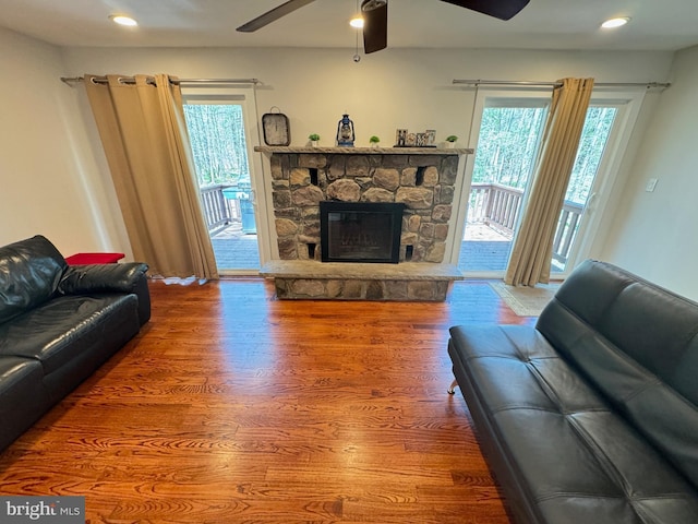 living room featuring hardwood / wood-style flooring, a stone fireplace, a healthy amount of sunlight, and ceiling fan