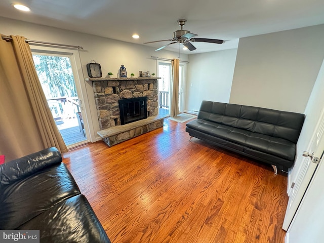 living room with hardwood / wood-style flooring, ceiling fan, plenty of natural light, and a stone fireplace