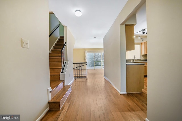 corridor featuring stairway, wood-type flooring, baseboards, and a sink