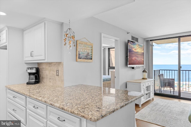 kitchen featuring white cabinetry, backsplash, light stone countertops, and expansive windows