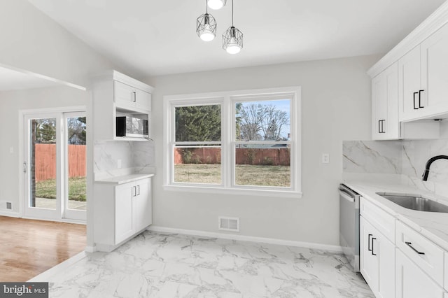 kitchen featuring tasteful backsplash, white cabinetry, sink, stainless steel dishwasher, and light stone counters