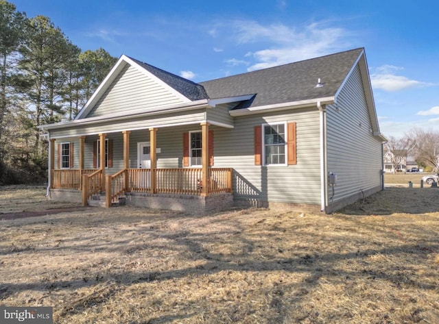 view of front facade with a porch, roof with shingles, and a front yard