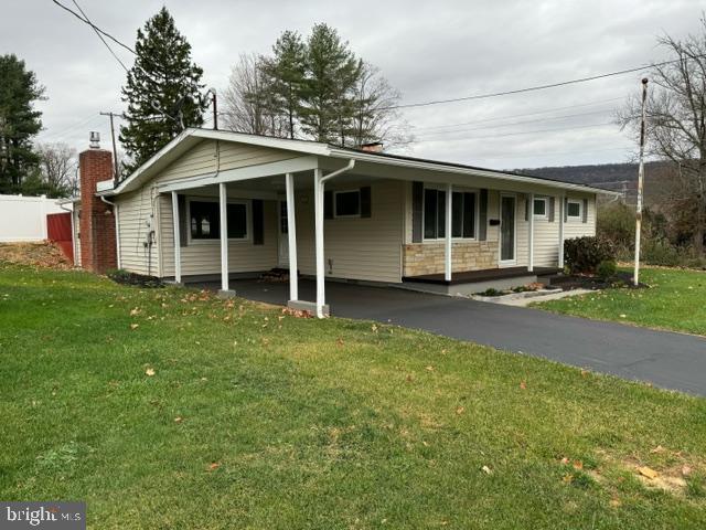 single story home with driveway, an attached carport, a front yard, and stone siding