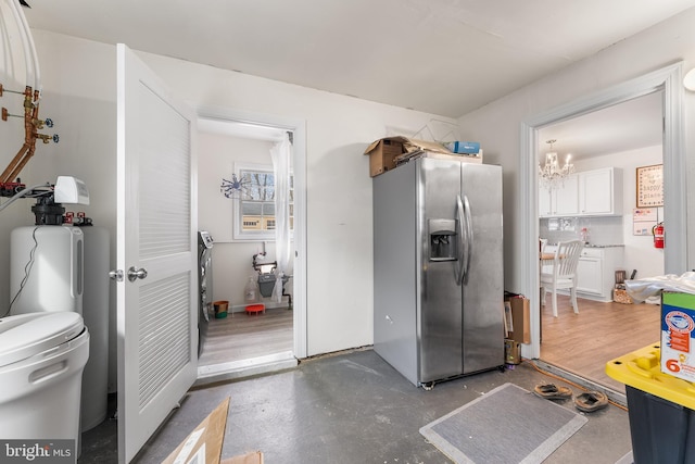 kitchen featuring concrete flooring, stainless steel fridge, a notable chandelier, and white cabinetry