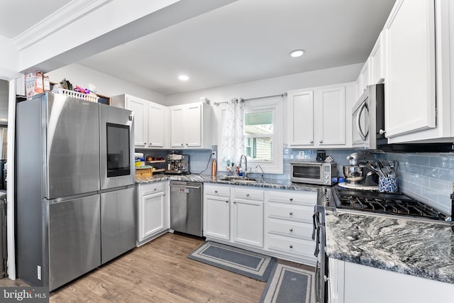 kitchen with dark stone counters, appliances with stainless steel finishes, wood finished floors, white cabinetry, and a sink